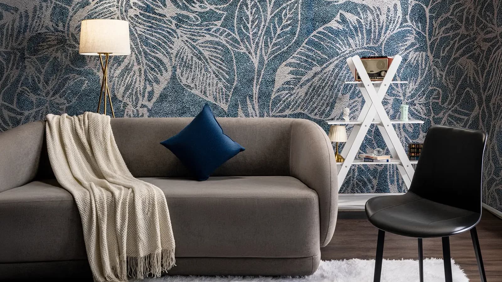A studio set with a sofa, a floor lamp and a leaf-print wall